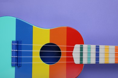Photo of Colorful ukulele on purple background, top view. String musical instrument