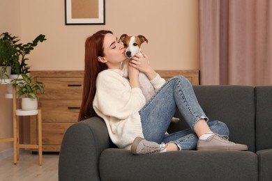 Photo of Woman kissing cute Jack Russell Terrier dog on sofa at home