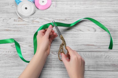 Photo of Woman cutting green ribbon with scissors at white wooden table, top view