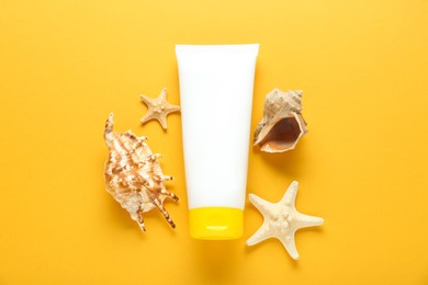 Photo of Suntan product, starfishes and seashells on orange background, flat lay