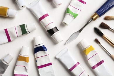 Photo of Brushes, spatula and paints on blank canvas, flat lay