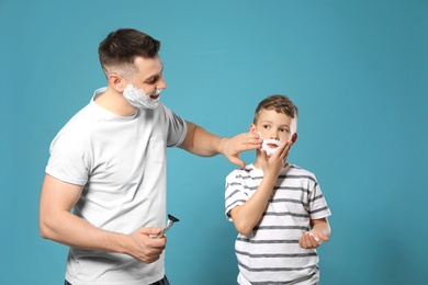 Photo of Dad applying shaving foam on son's face against blue background