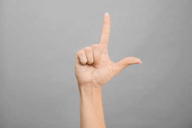 Photo of Woman showing L letter on grey background, closeup. Sign language