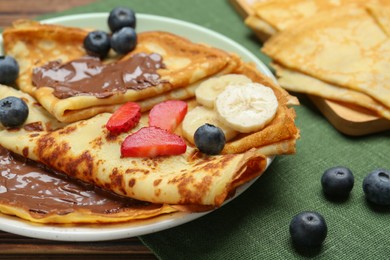 Photo of Tasty crepes with chocolate paste, banana and berries served on table, closeup