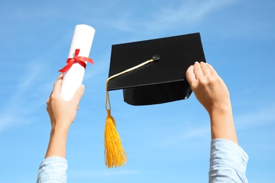 Student with graduation hat and diploma against blue sky, closeup