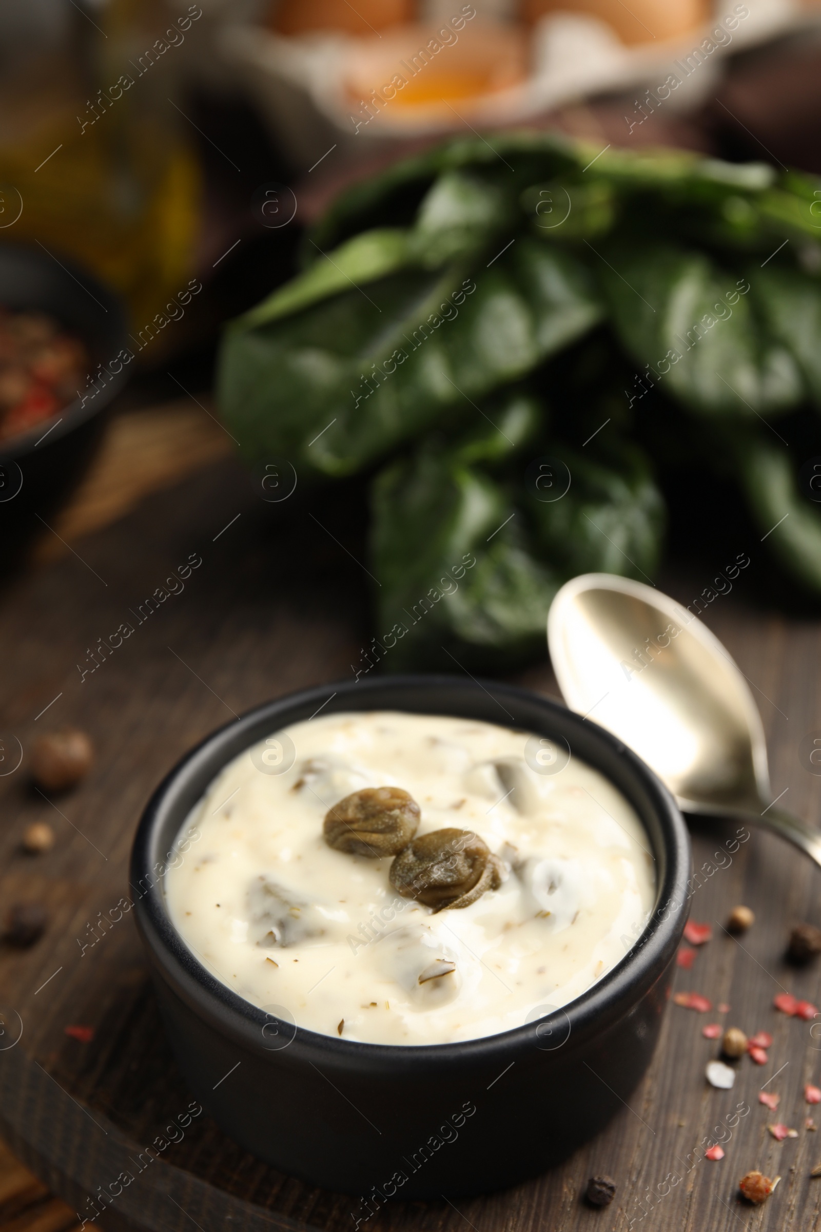 Photo of Caper sauce in bowl on wooden board, closeup