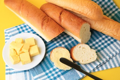 Photo of Whole and cut baguettes with fresh butter on yellow background, above view