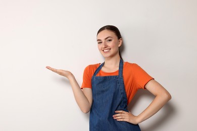 Beautiful young woman in clean denim apron on light grey background. Space for text