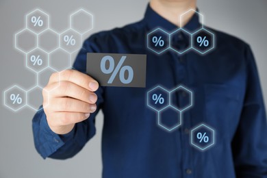 Image of Man showing business card with percent sign on light grey background, closeup. Discount concept