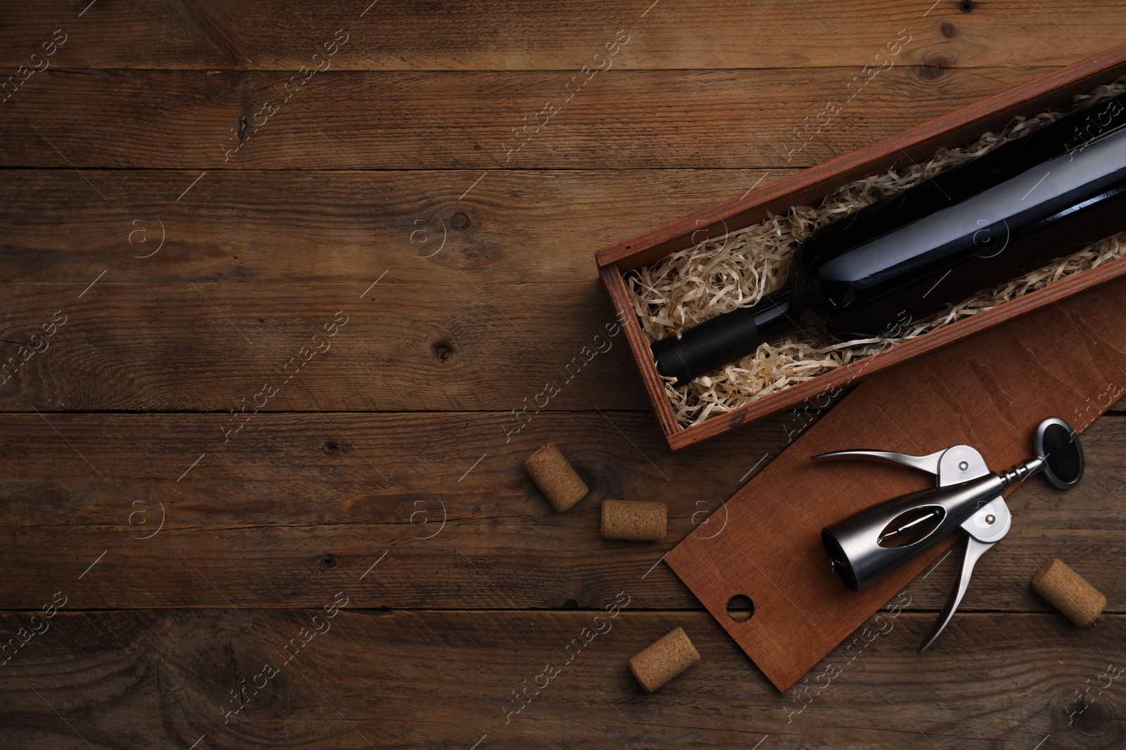 Photo of Box with wine bottle, wing corkscrew and corks on wooden table, flat lay. Space for text