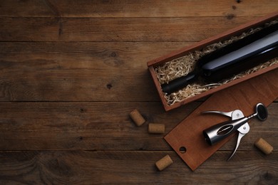 Box with wine bottle, wing corkscrew and corks on wooden table, flat lay. Space for text