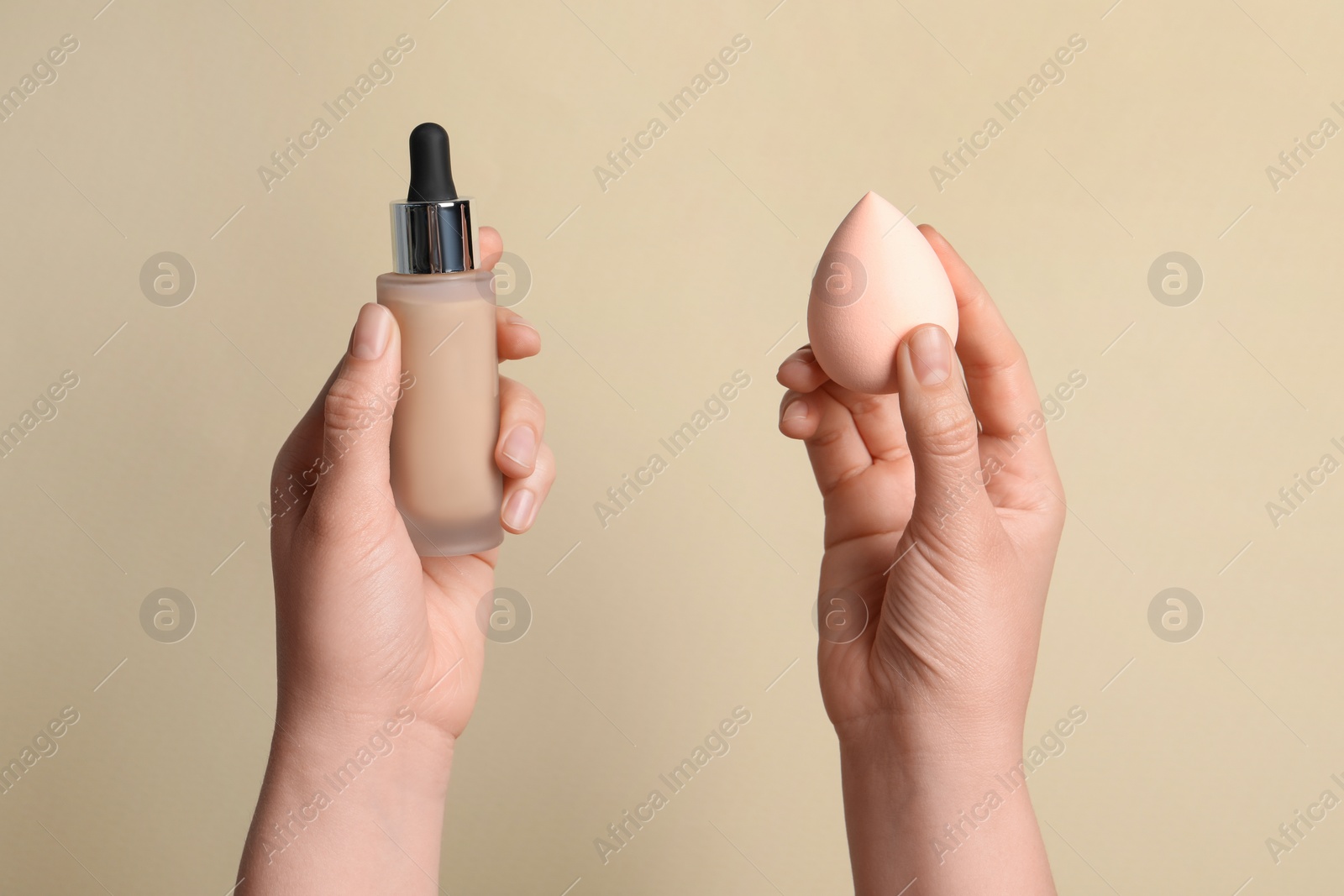 Photo of Woman holding bottle with skin foundation and makeup sponge on beige background, closeup