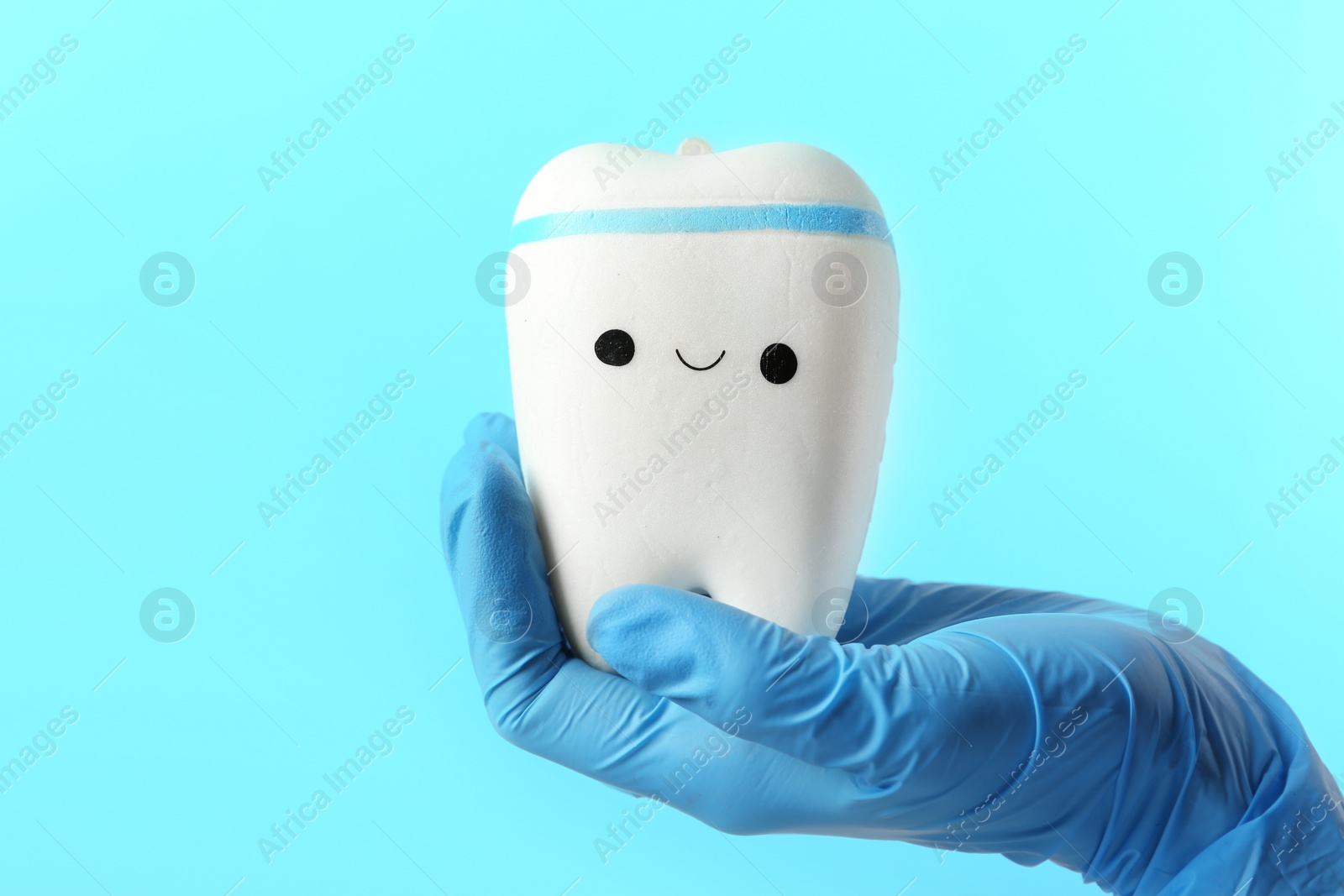 Photo of Dentist holding model of tooth with cute face on color background