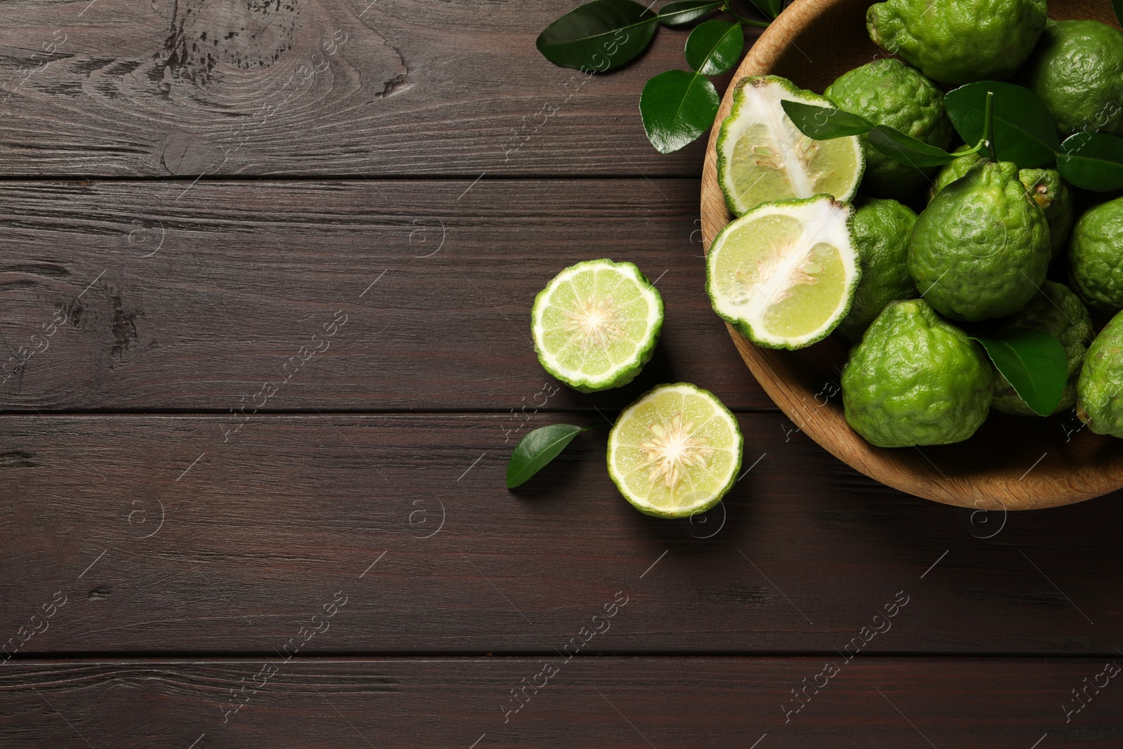 Photo of Whole and cut ripe bergamot fruits with green leaves on wooden table, flat lay. Space for text