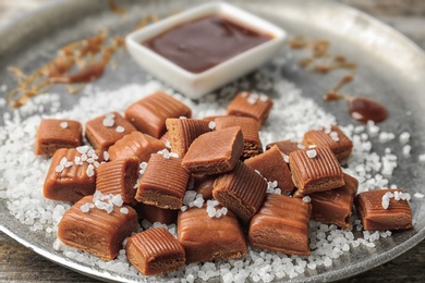 Photo of Delicious caramel candies, sauce and salt on plate, closeup