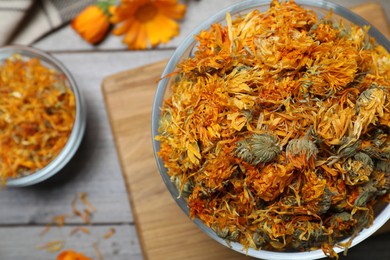 Glass bowl with dry calendula flowers on wooden table, top view. Space for text