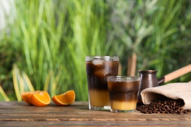 Tasty refreshing drink with coffee and orange juice on wooden table against blurred background, space for text