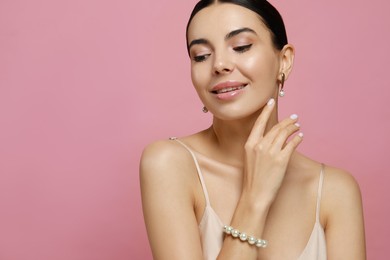 Young woman wearing elegant pearl jewelry on pink background, closeup. Space for text