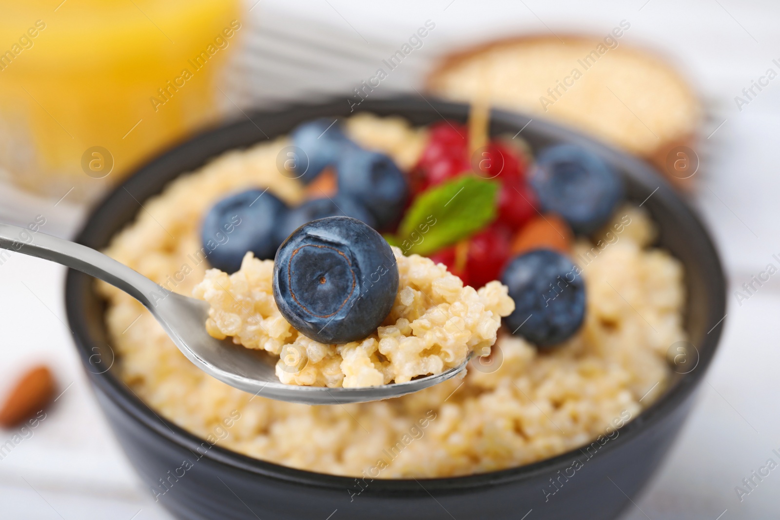 Photo of Spoon of delicious cooked quinoa with blueberry above bowl, closeup