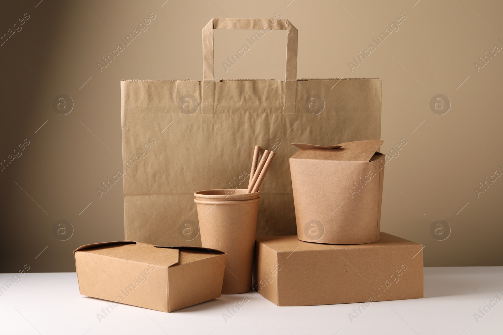 Photo of Eco friendly food packaging. Paper containers, bag and straws on white table against beige background