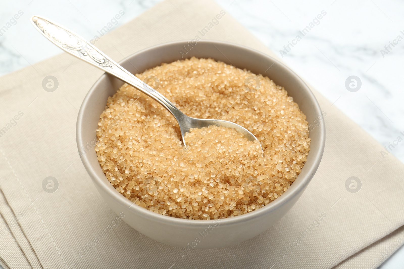 Photo of Brown sugar in bowl and spoon on white marble table, closeup