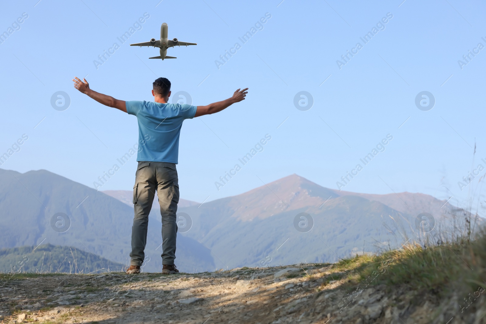 Image of Man looking at airplane flying in sky over mountains, back view