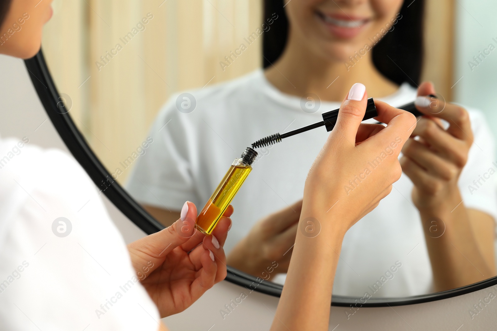 Photo of Young woman with eyelash oil near mirror, closeup