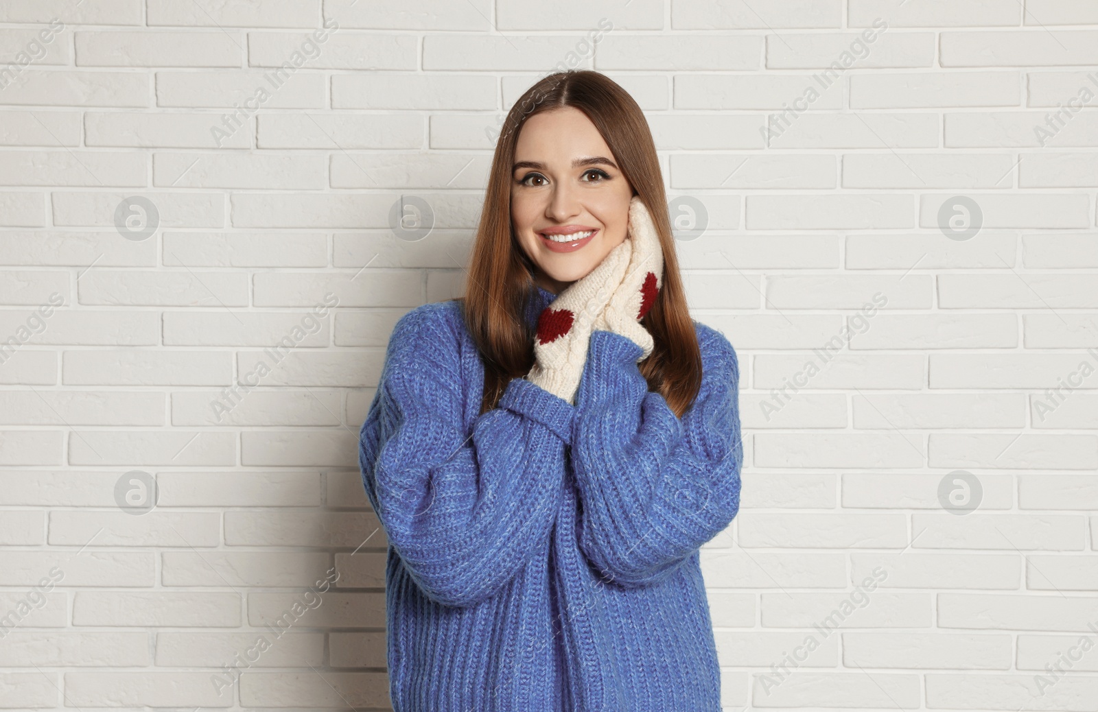 Photo of Beautiful young woman in mittens and blue sweater near white brick wall. Winter season