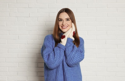 Photo of Beautiful young woman in mittens and blue sweater near white brick wall. Winter season