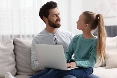 Photo of Happy man and his daughter with laptop on sofa at home