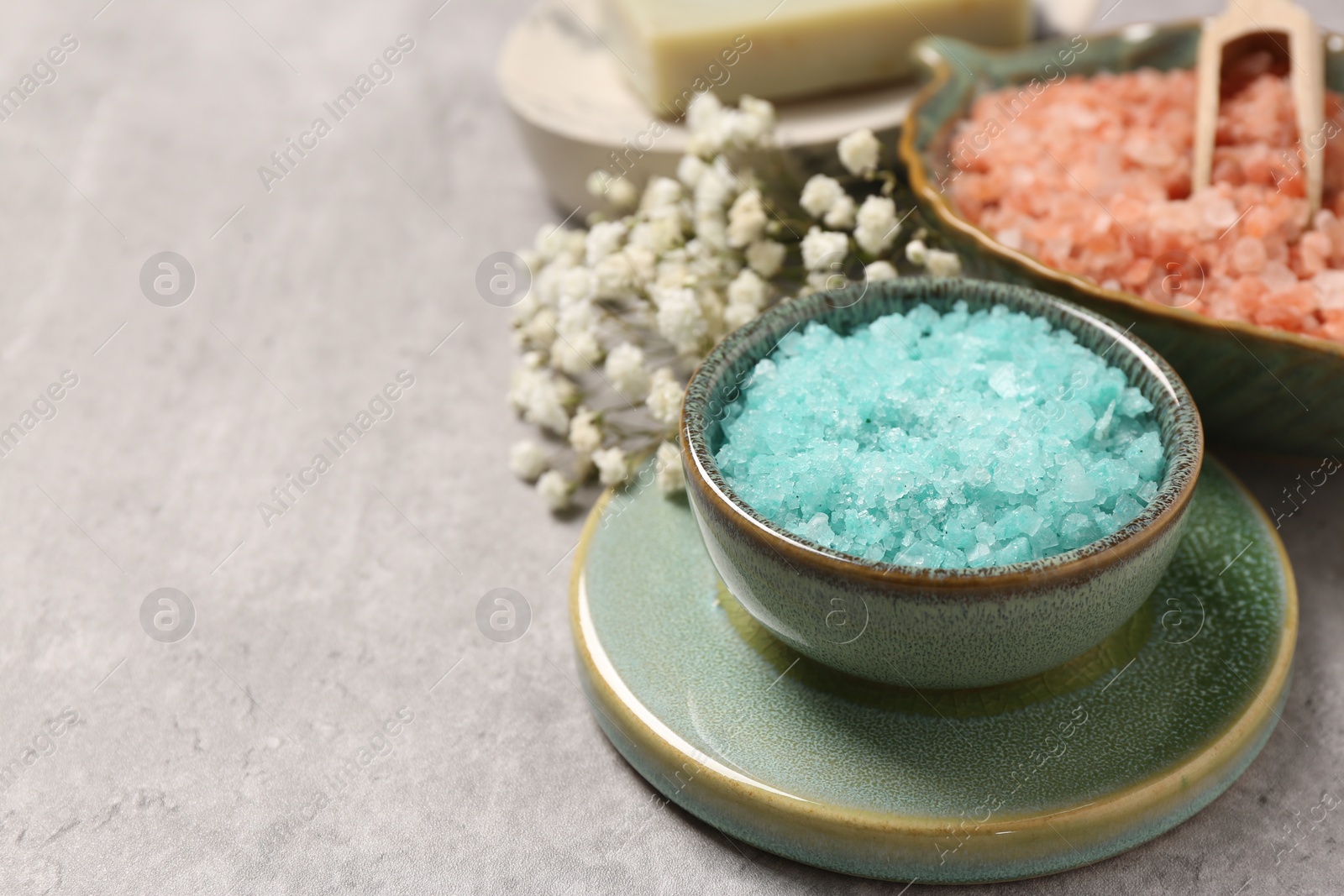Photo of Colorful sea salt and beautiful flowers on light grey table, closeup. Space for text