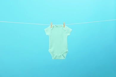 Baby onesie hanging on clothes line against blue background. Laundry day