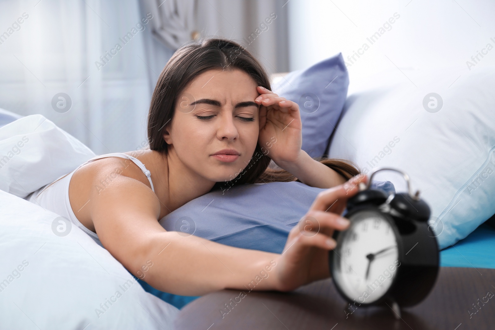 Photo of Young woman turning off alarm clock in morning. Bedtime