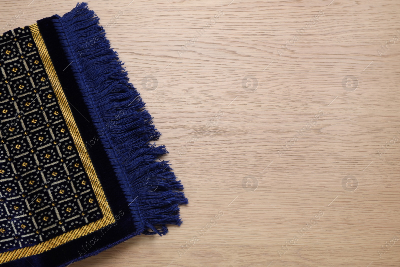 Photo of Muslim prayer rug on wooden table, top view. Space for text