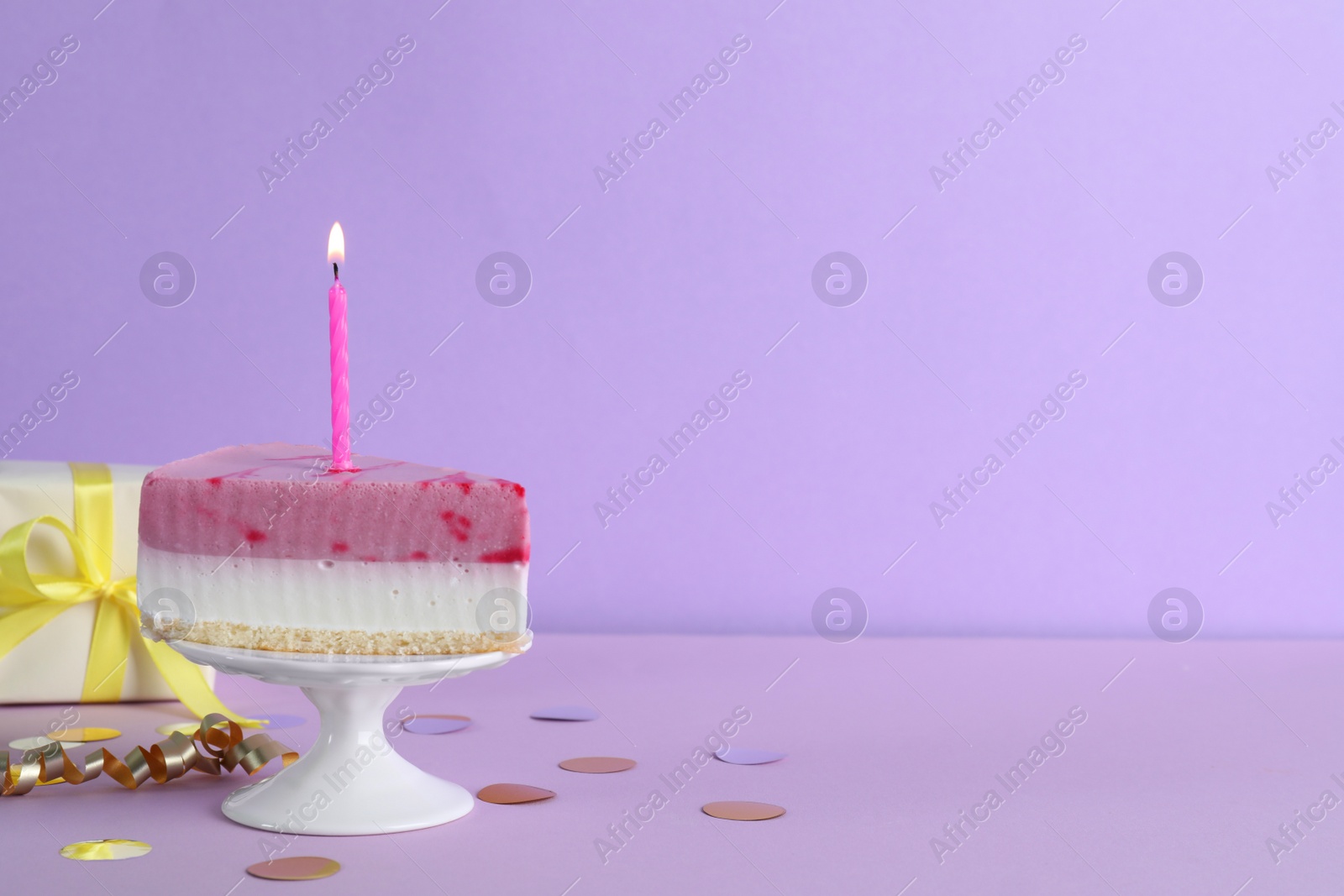 Photo of Piece of delicious birthday cake with candle near gift box on violet background, space for text
