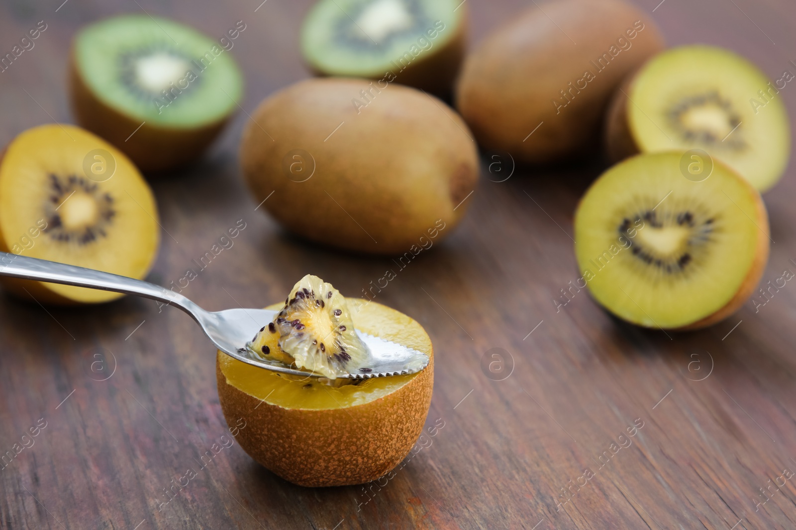 Photo of Spoon with half of kiwi and fruits on wooden table, closeup. Space for text