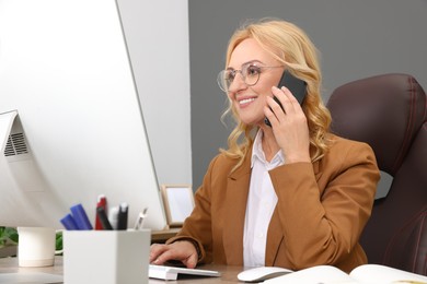 Photo of Lady boss talking on smartphone near computer at desk in office. Successful businesswoman