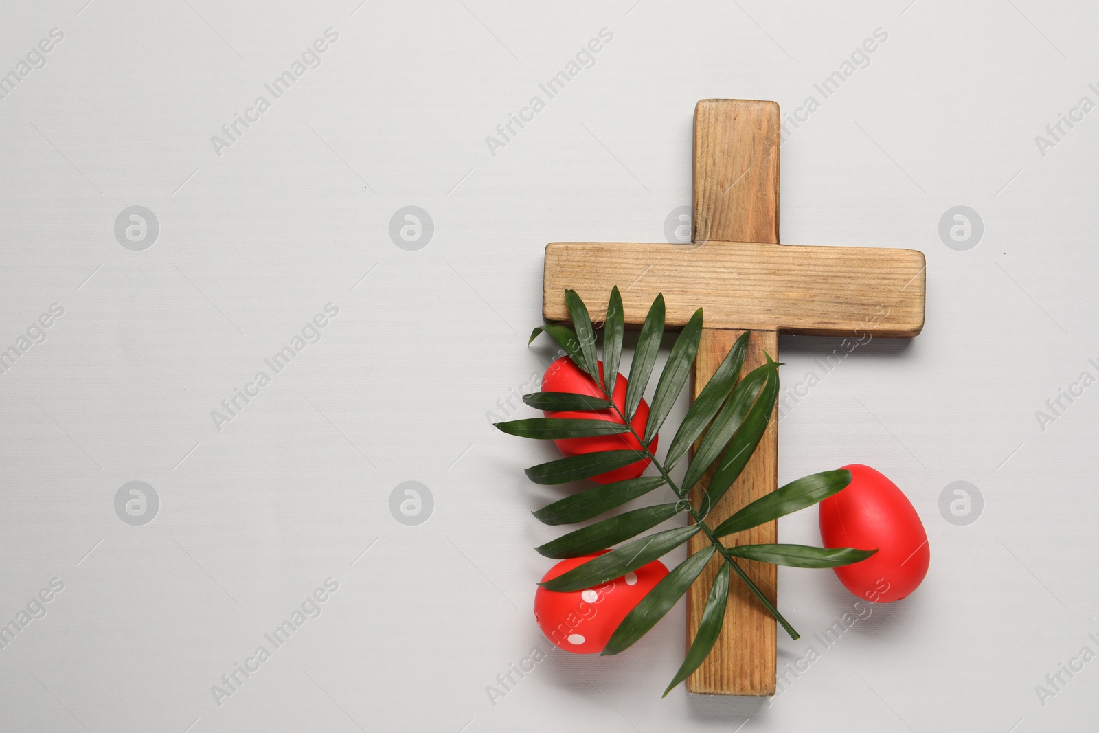 Photo of Wooden cross, painted Easter eggs and palm leaf on light grey background, flat lay. Space for text