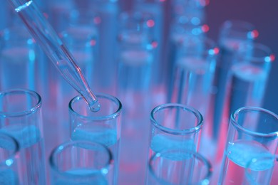 Dripping liquid from pipette into test tube on color background, closeup