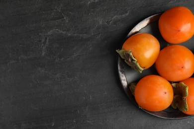 Photo of Tasty ripe persimmons on black slate table, top view. Space for text