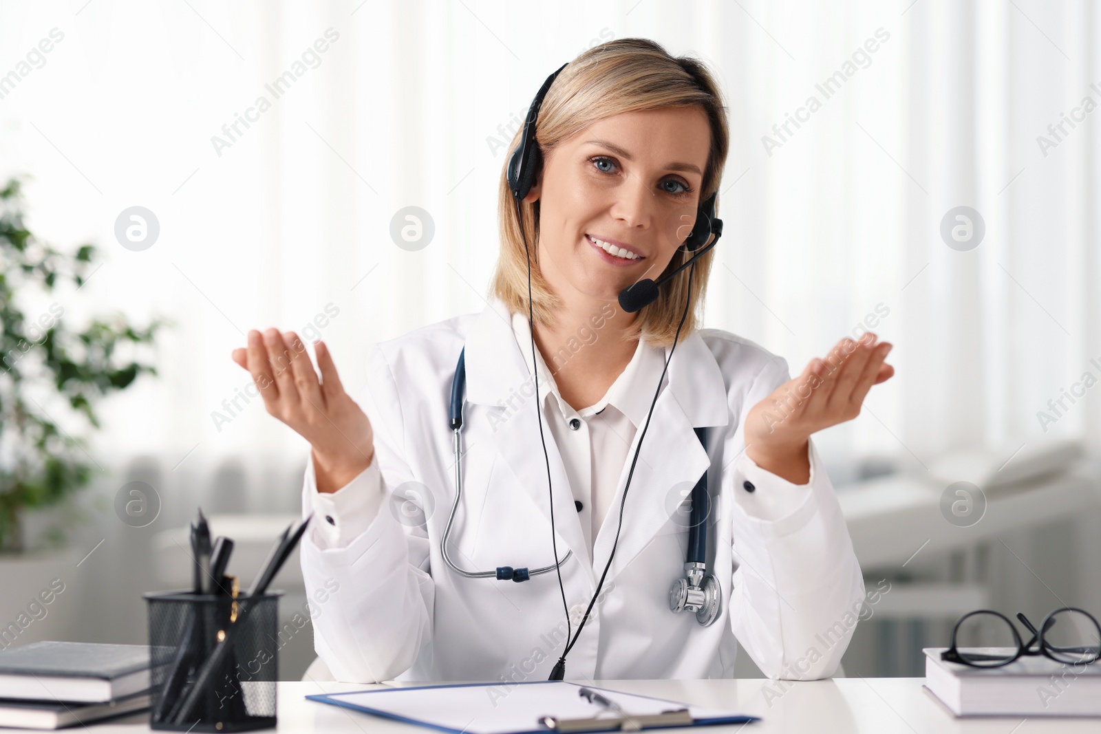 Photo of Smiling doctor in headphones having online consultation at table indoors