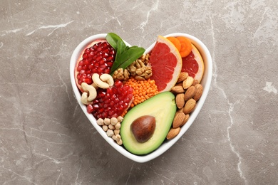 Photo of Bowl with products for heart-healthy diet on color background, top view