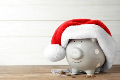 Photo of Piggy bank with Santa hat and money on wooden table, space for text