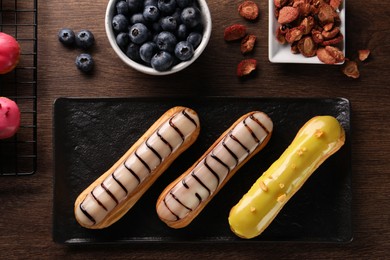 Different tasty glazed eclairs, dry strawberries and blueberries on wooden table, flat lay