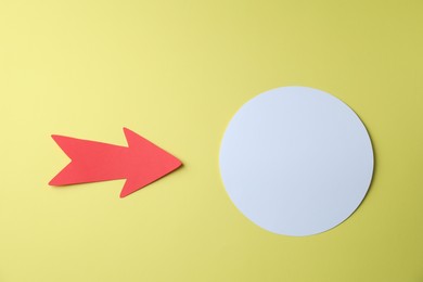 Red paper arrow and white circle on yellow background, flat lay. Space for text