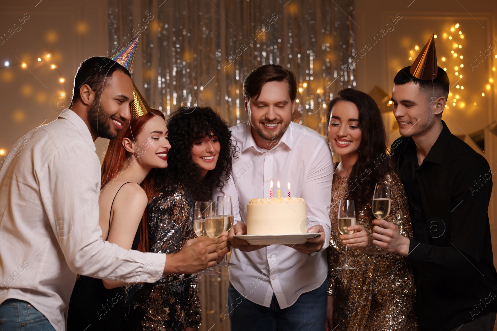 Photo of Happy friends with tasty cake and glasses of sparkling wine celebrating birthday indoors