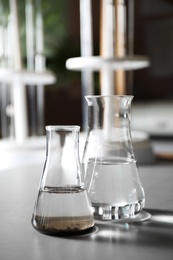 Photo of Glassware with soil extract and water on grey table. Laboratory research