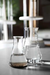 Glassware with soil extract and water on grey table. Laboratory research