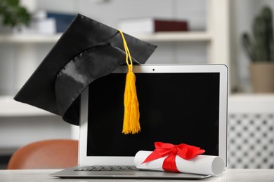 Graduation hat, student's diploma and laptop on white table indoors