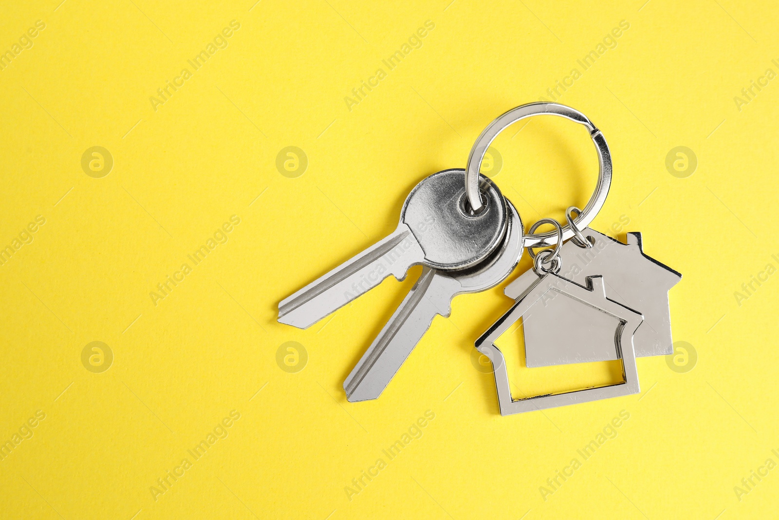 Photo of Keys with keychain in shape of house on yellow background, top view. Space for text